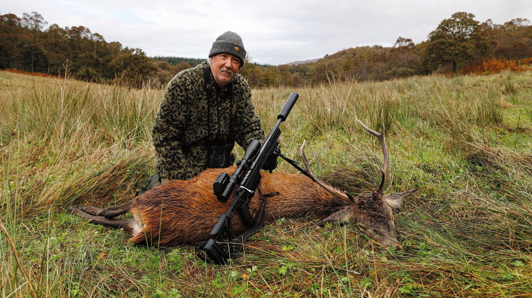 Bruce Potts kneeling beside a red stag on wet Argyll hill ground with the Tikka T3x Ace Game